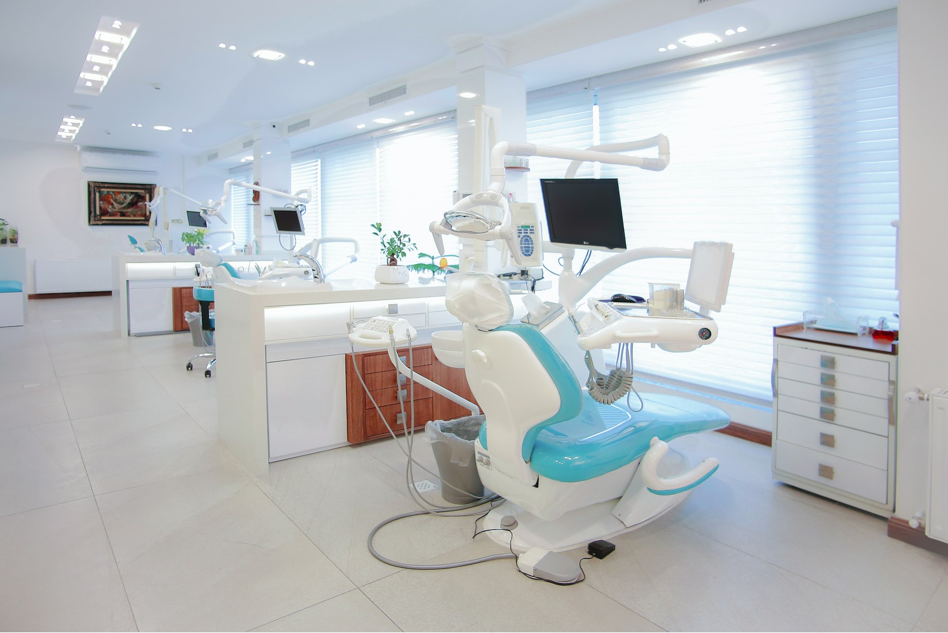 Gabinete de la clínica: sillón dental, monitor y armarios blancos con luz natural.